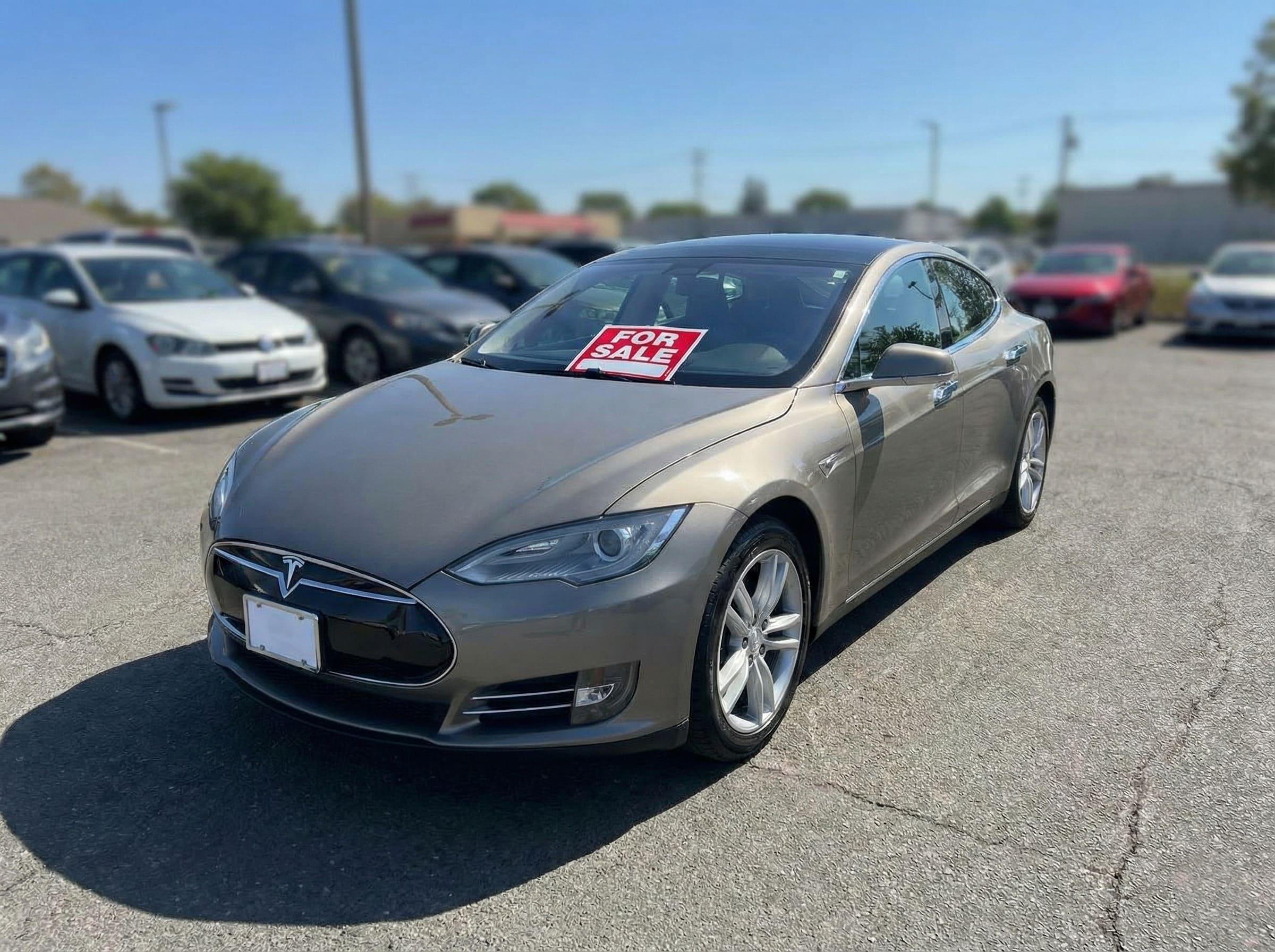 A used electric vehicle parked in a lot with a price tag on the windshield